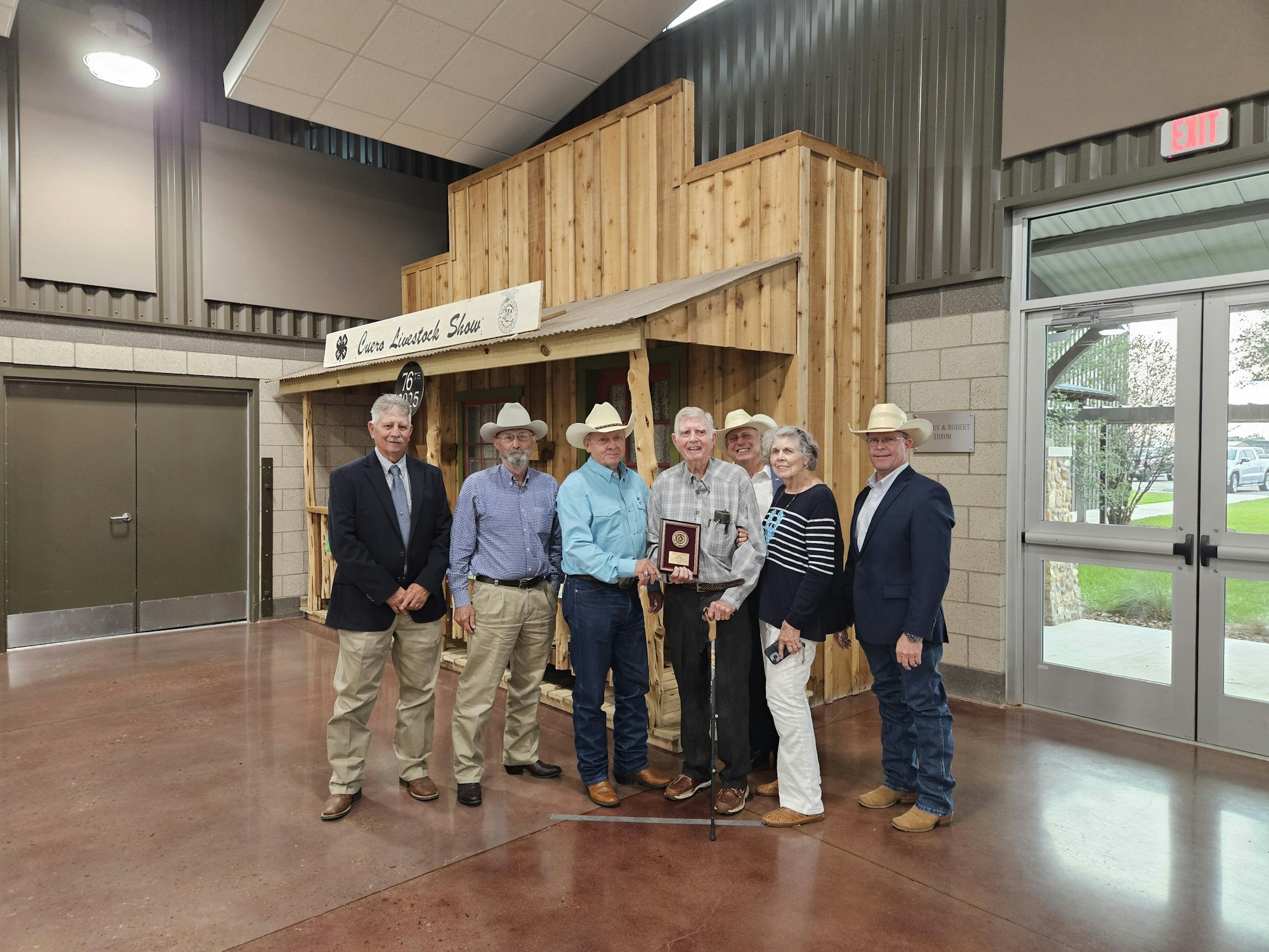 A group of people, some in cowboy hats, pose with a plaque in front of a "Livestock Show" sign.