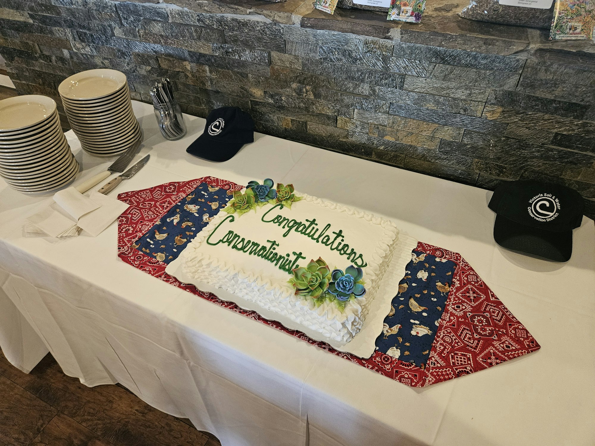 A cake with "Congratulations Conservationists" on a decorated table with hats, plates, and utensils.