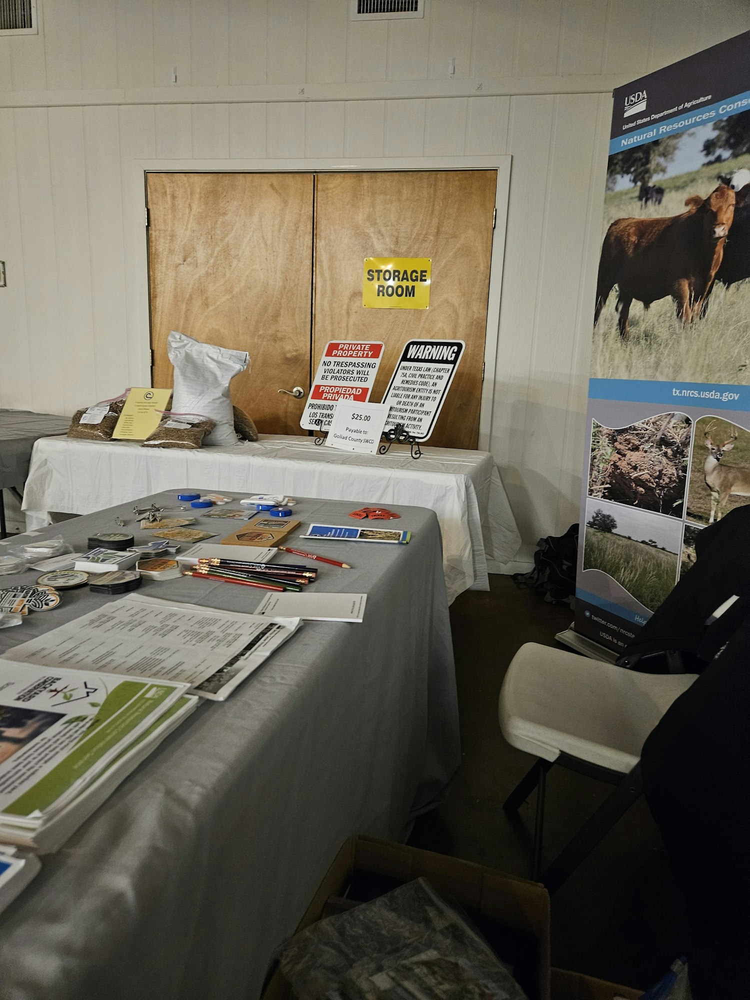 A table with various papers, promotional items, warning signs, and a USDA display banner near a door labeled "Storage Room."