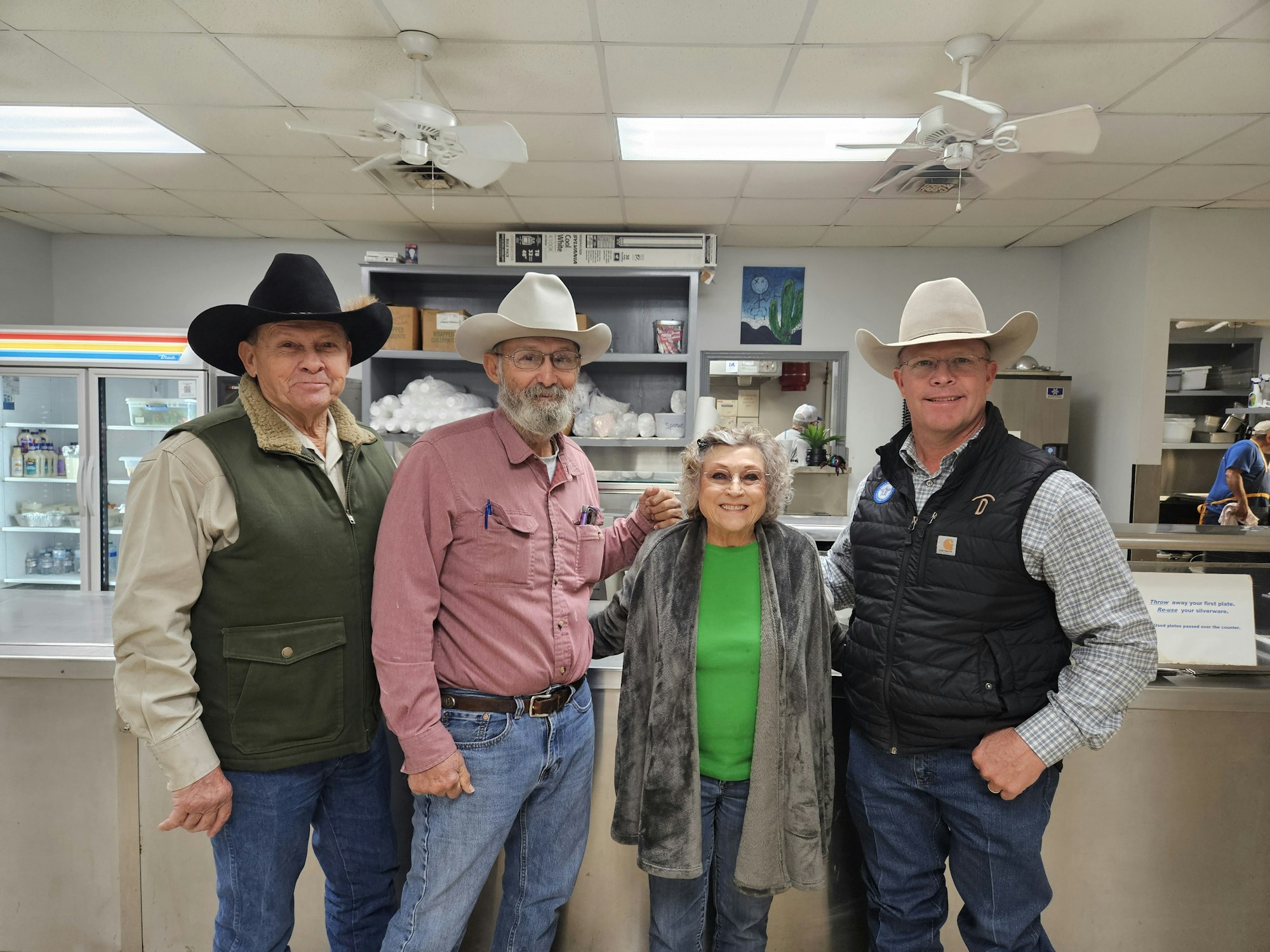 Four people, dressed in cowboy attire, pose together in a kitchen setting. Warm smiles and a friendly atmosphere highlight the scene.