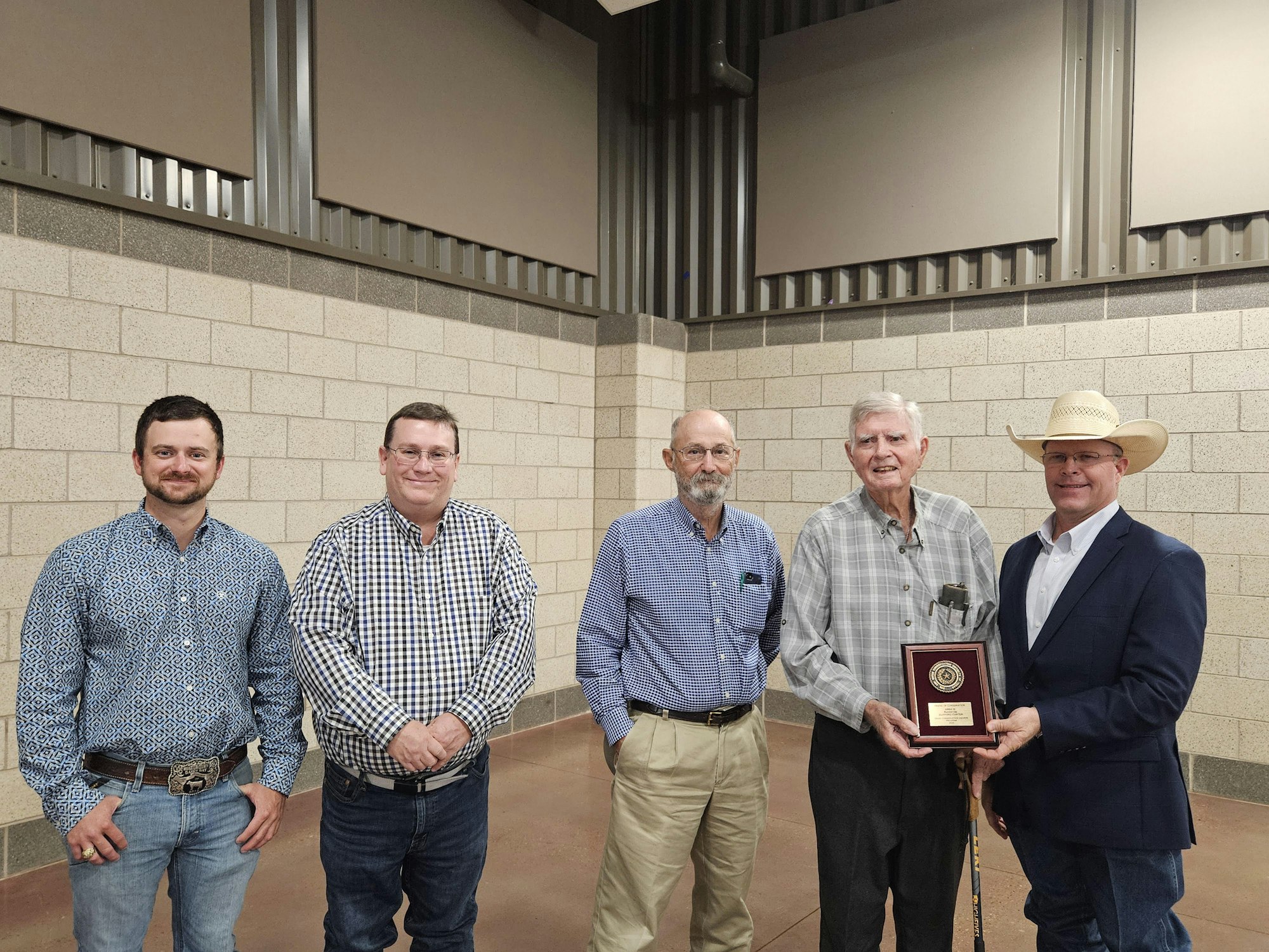 Five men posing indoors; one holds a plaque.