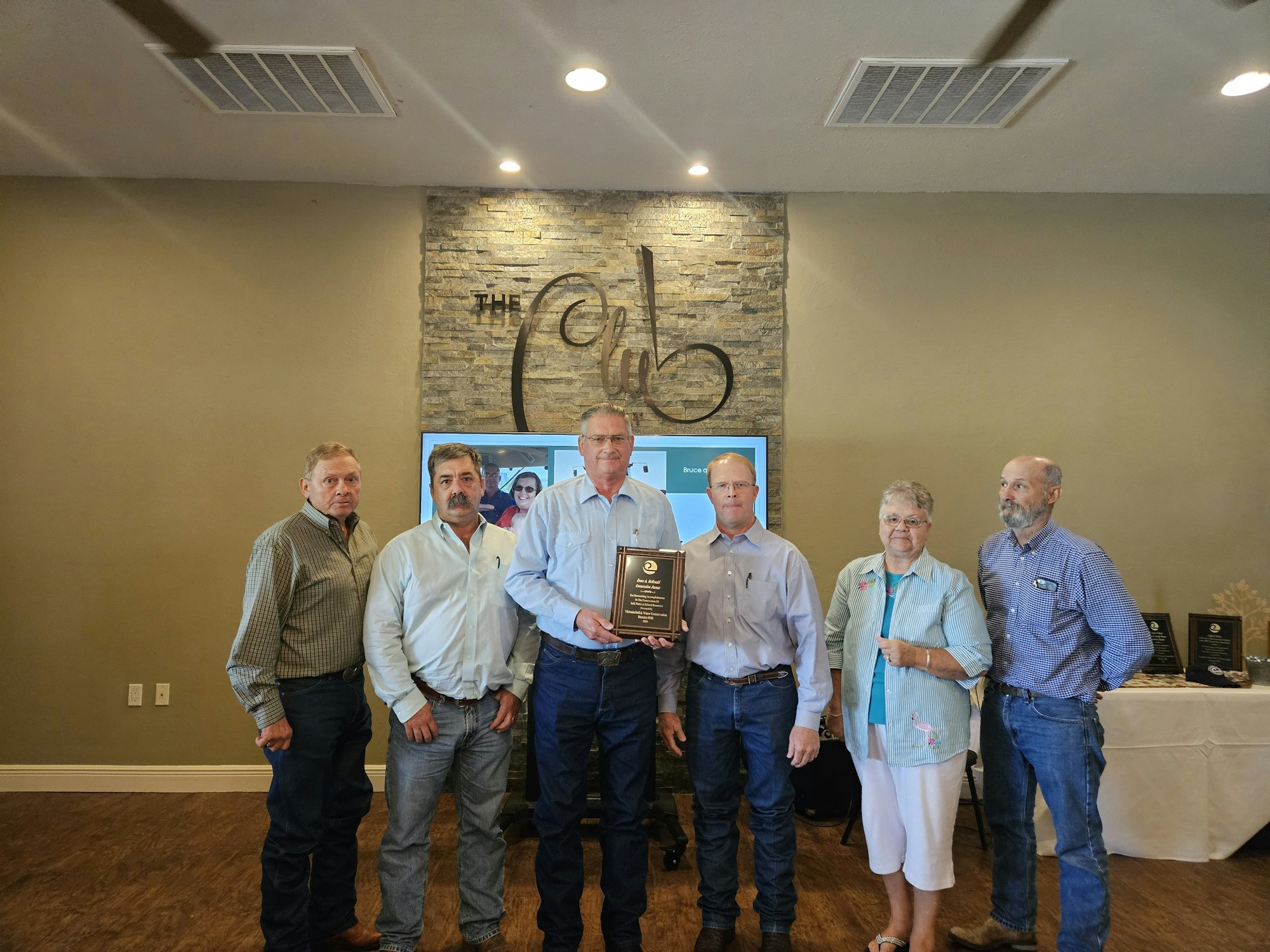 A group of people posing indoors, one holding a plaque with awards displayed behind them.