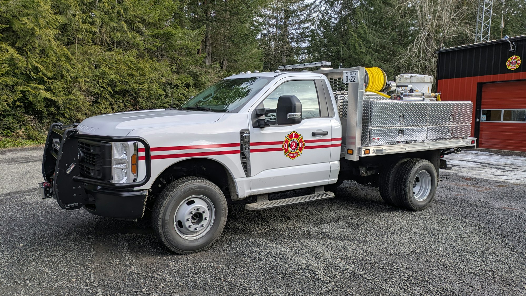 Fire department utility vehicle with equipment in a forested area, parked near a building.