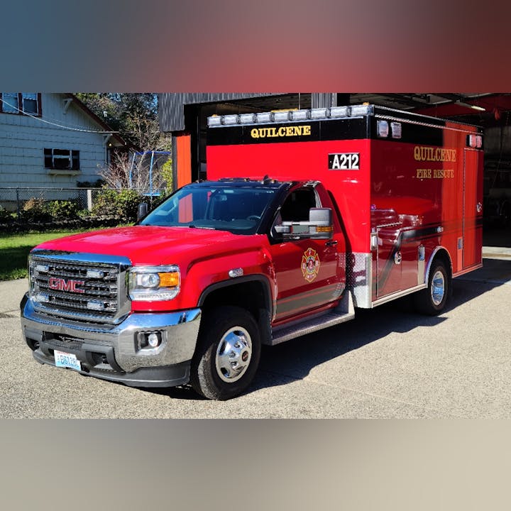 A red GMC fire rescue vehicle labeled "Quilcene Fire Rescue," parked outside a building.