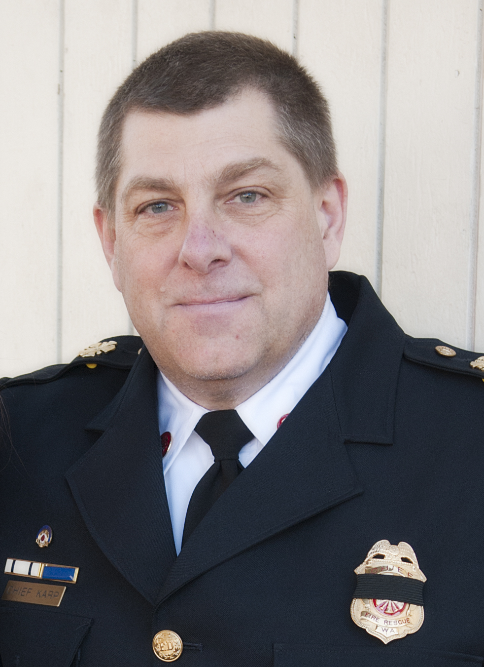 A person in a uniform with badges and a name tag, standing in front of a light background.