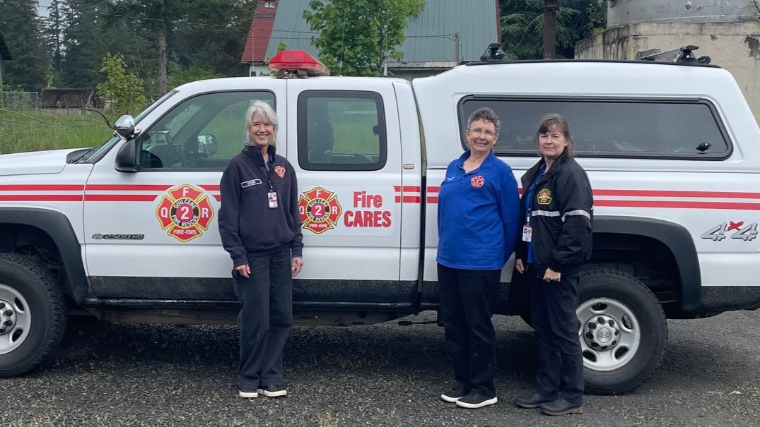 Three people standing next to a fire department vehicle labeled "Fire CARES" with Department logos.