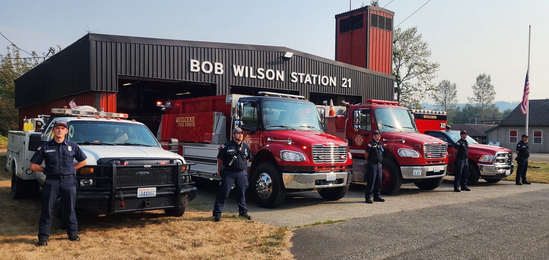 Firefighters stand in front of Bob Wilson Station 21 with multiple fire trucks parked outside.