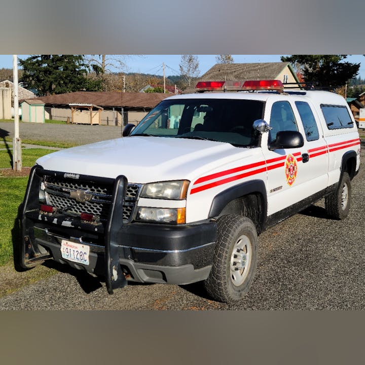 A white Chevrolet vehicle with red emergency stripes, equipped with a light bar, likely serving as a fire department vehicle.