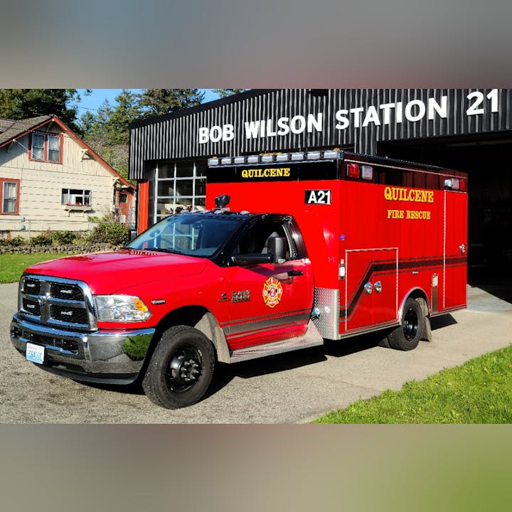 A red fire rescue vehicle parked outside Bob Wilson Station 21 in Quilcene, with a house visible in the background.
