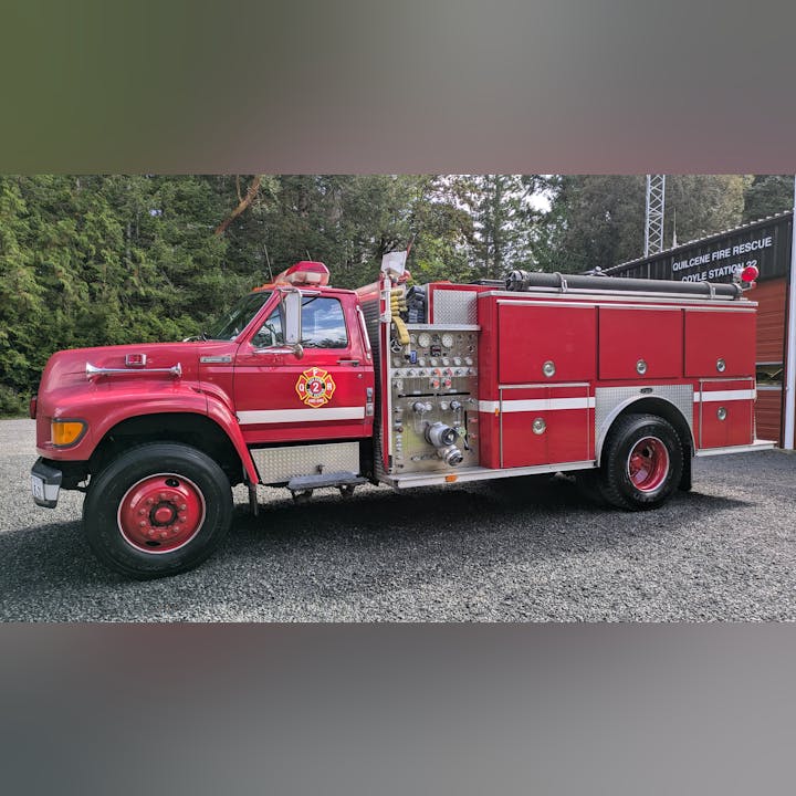 Red fire truck parked outside a fire station with trees in the background.