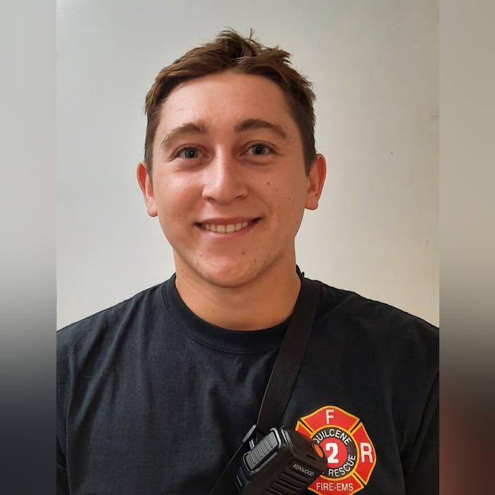 A smiling person in a fire department shirt holding a walkie-talkie.