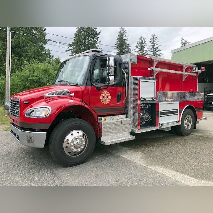 A bright red fire truck parked outside, featuring various compartments and equipment for firefighting.