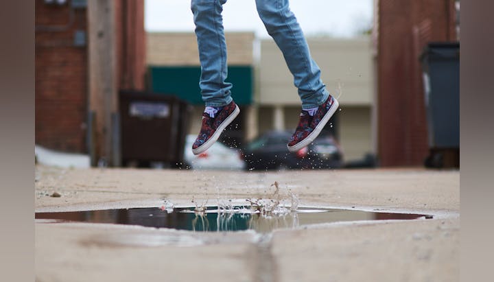 Person jumping over a puddle on a city street, mid-air with a splash.