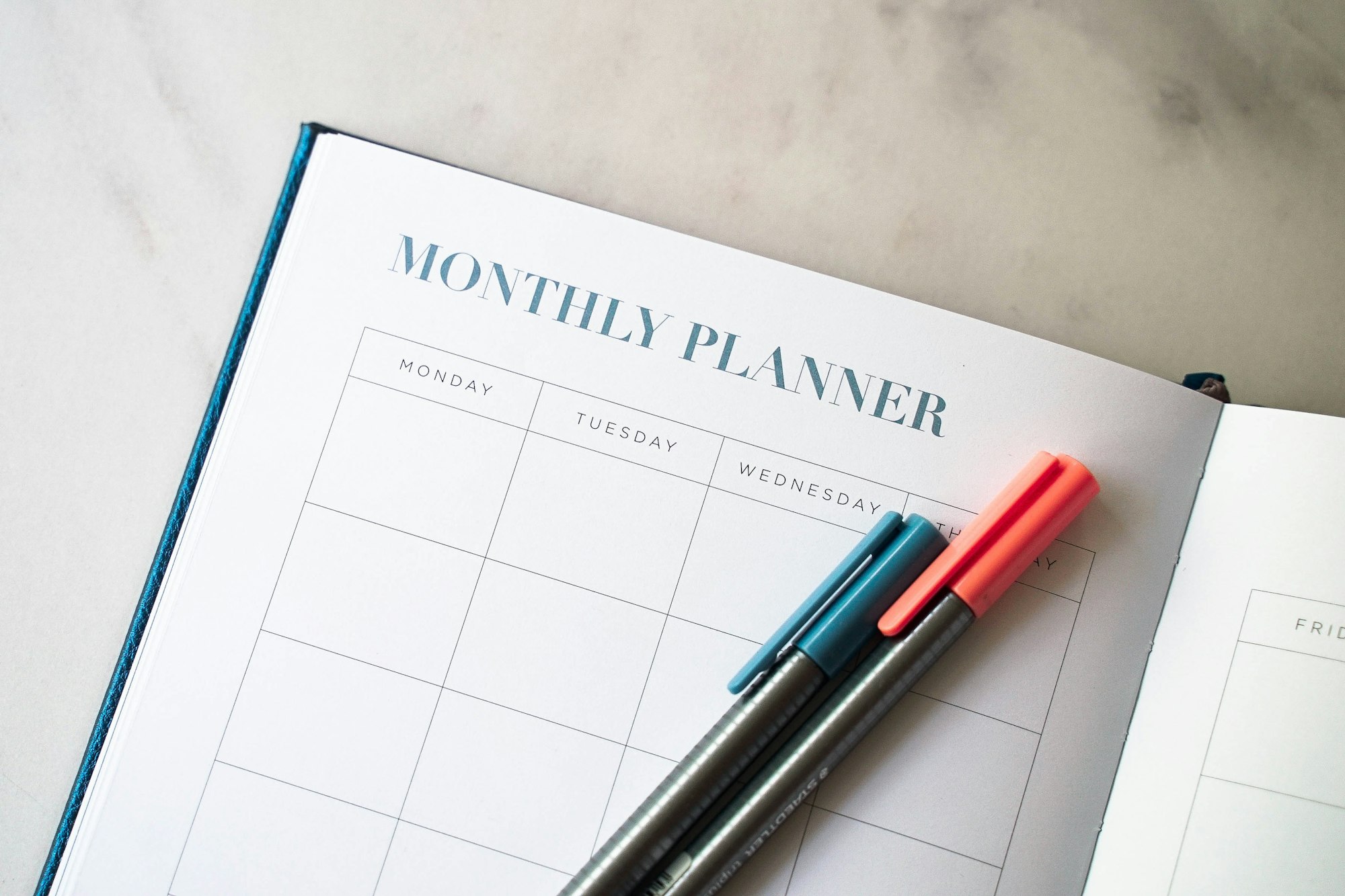 Photo of a monthly planner/calendar book with pens resting on open page