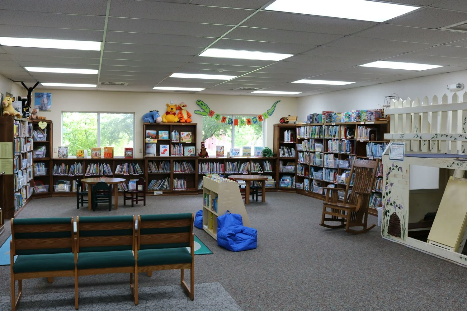 A cozy children's library with bookshelves, toys, small tables, chairs, and colorful decorations.