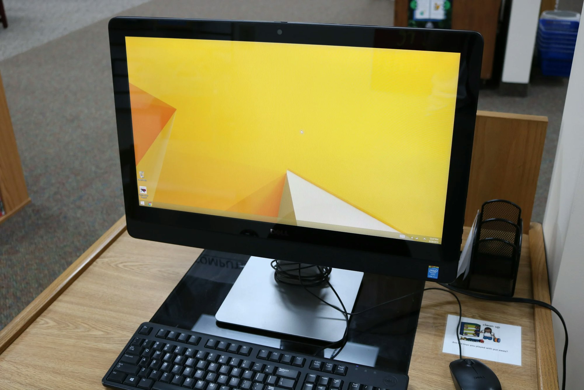 A desktop computer with a yellow geometric wallpaper, keyboard, and mouse on a wooden desk.