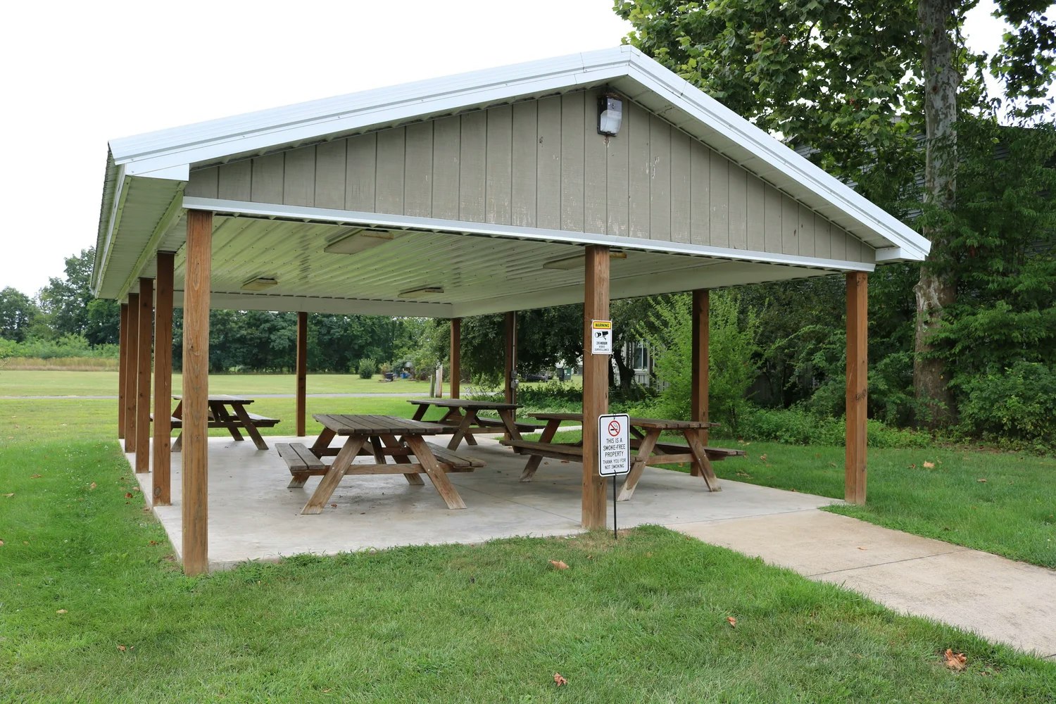 Covered picnic area with wooden tables, located in a grassy park setting.