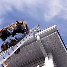 Person climbing a ladder onto a roof, clear sky in the background.