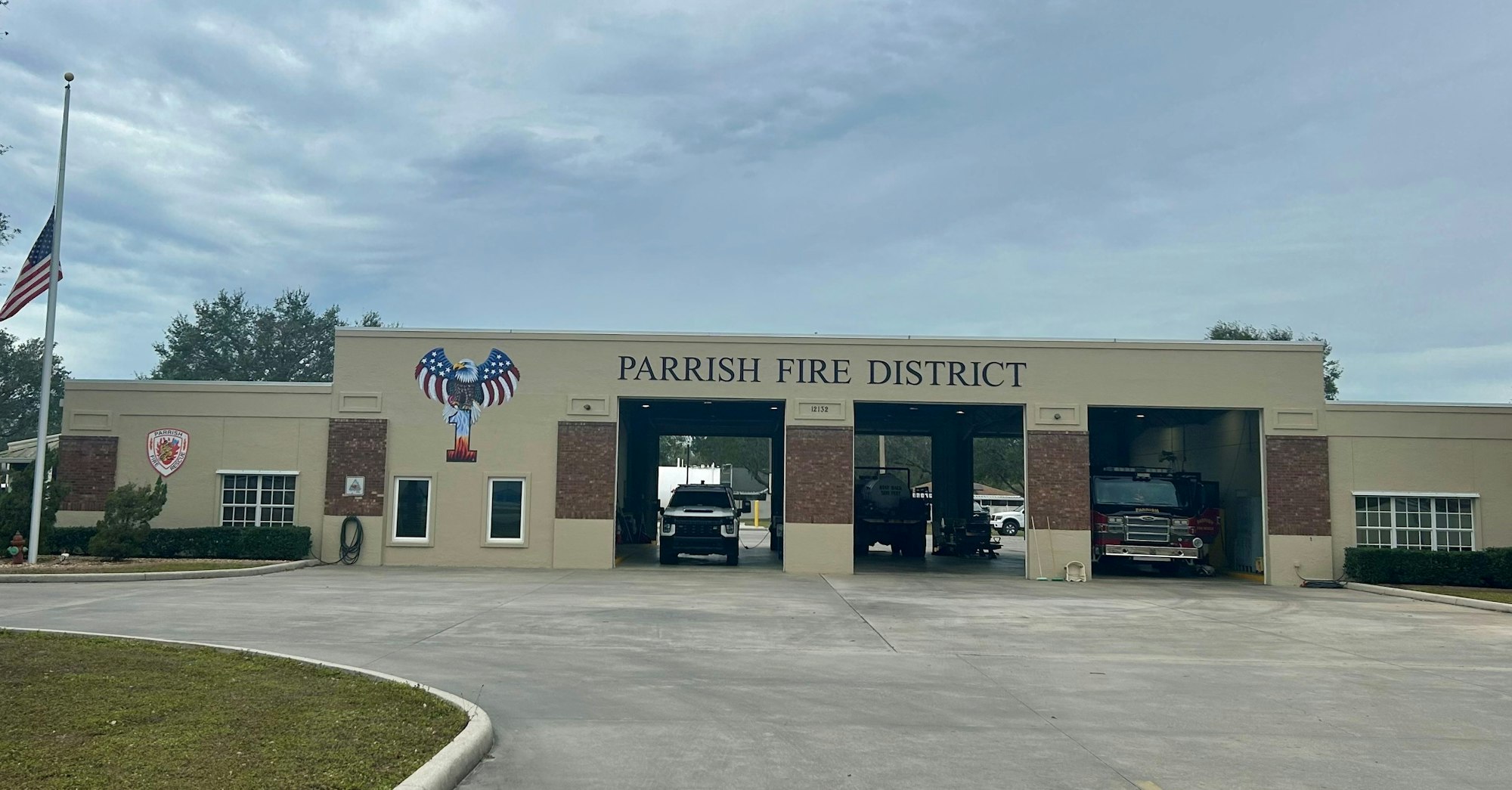 A fire station labeled "Parrish Fire District" with fire trucks inside and an American flag outside.