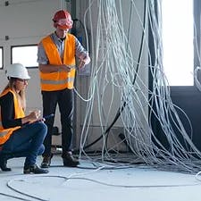 Two construction workers inspecting a bundle of messy cables on a job site.