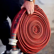 A hand holding a neatly rolled red fire hose connected to a hydrant.