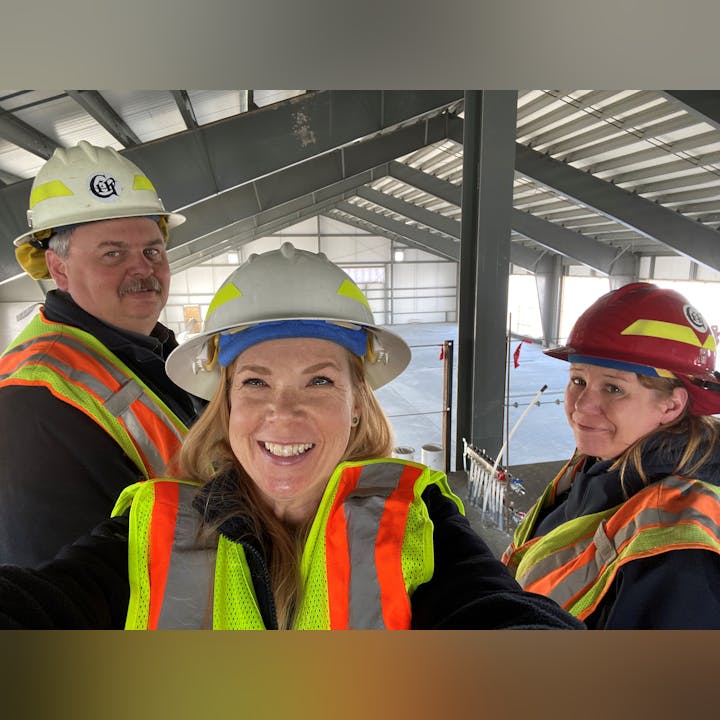 A group of three construction workers in safety gear, including hard hats and vests, taking a selfie in a building under construction.