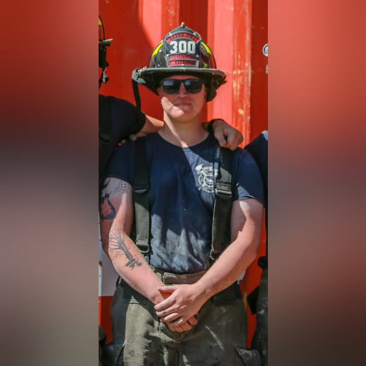 A firefighter with sunglasses and a helmet standing in front of a red surface.