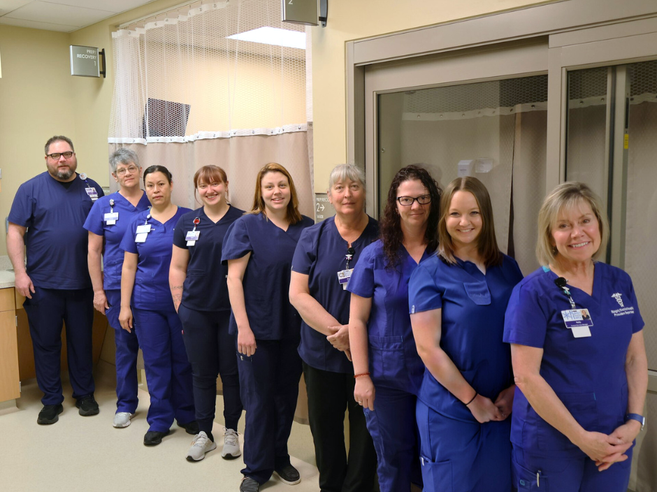 A group of healthcare professionals in blue scrubs standing in a hospital setting, smiling at the camera.