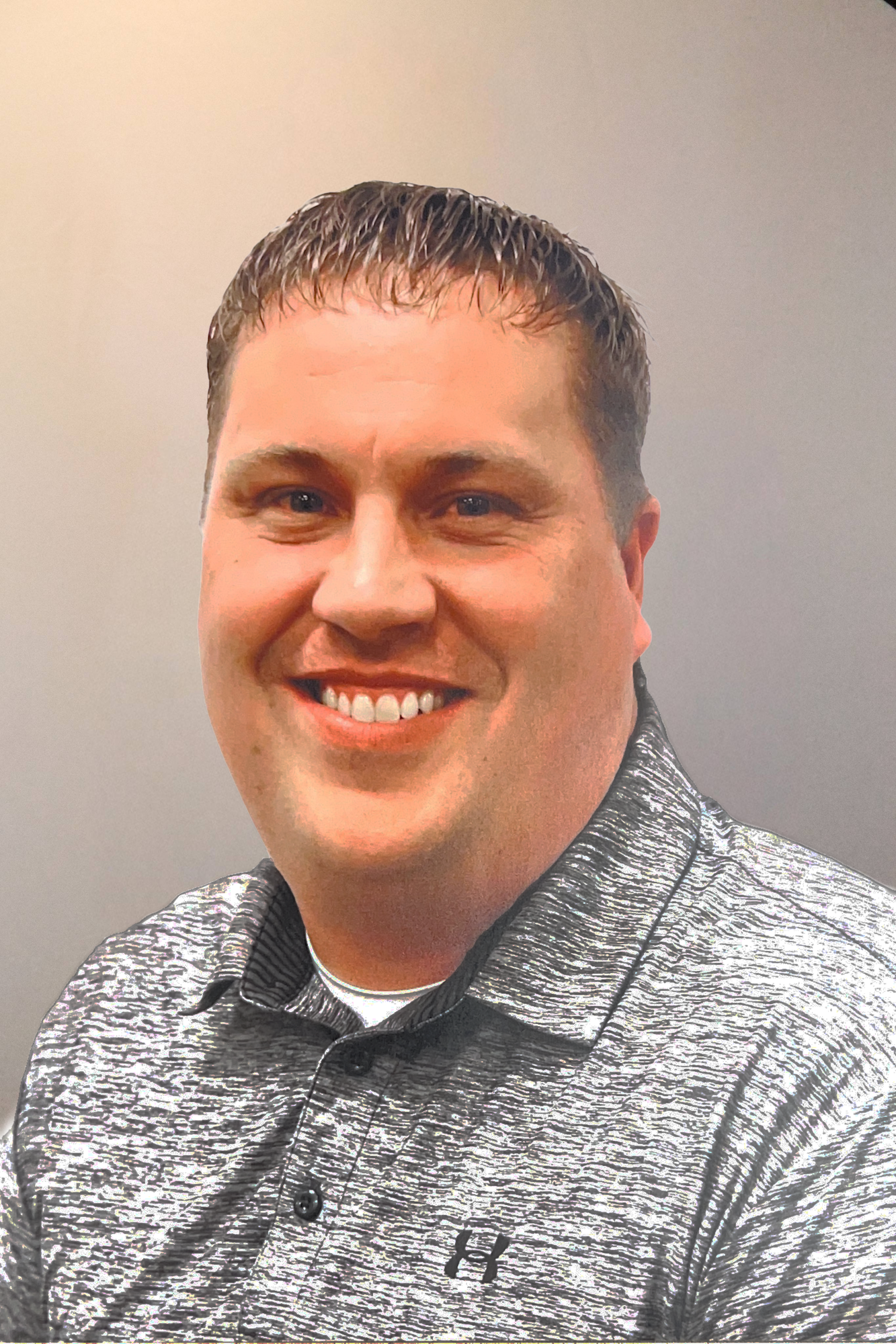 A person smiling, wearing a grey shirt with a black logo, against a neutral background.