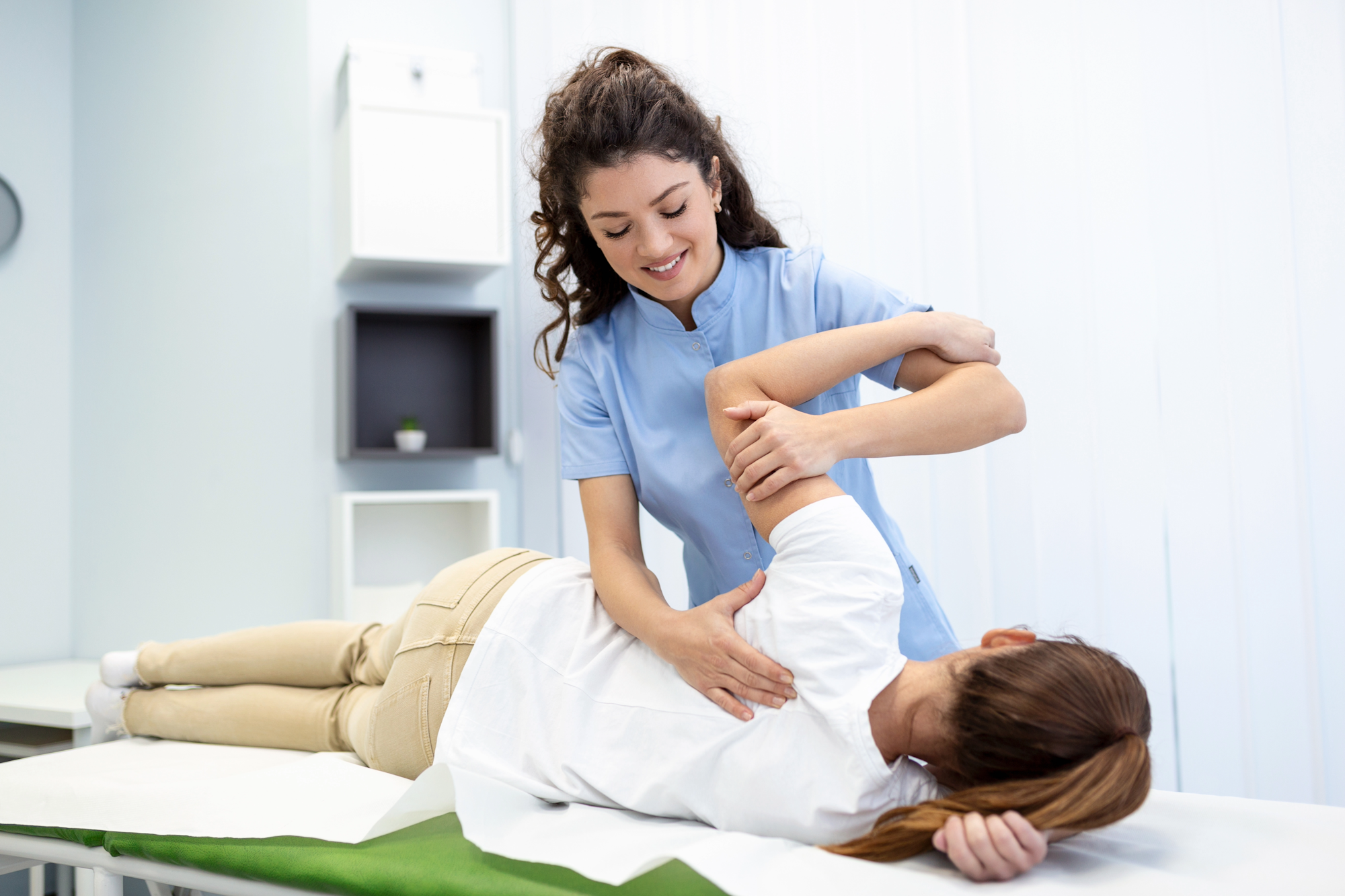 A physical therapist assists a patient lying on their side, focusing on arm and back therapy.