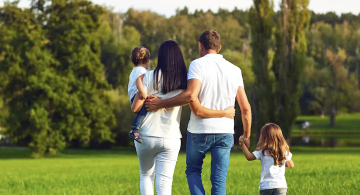 A family of four walking in a park, holding hands and enjoying a sunny day.