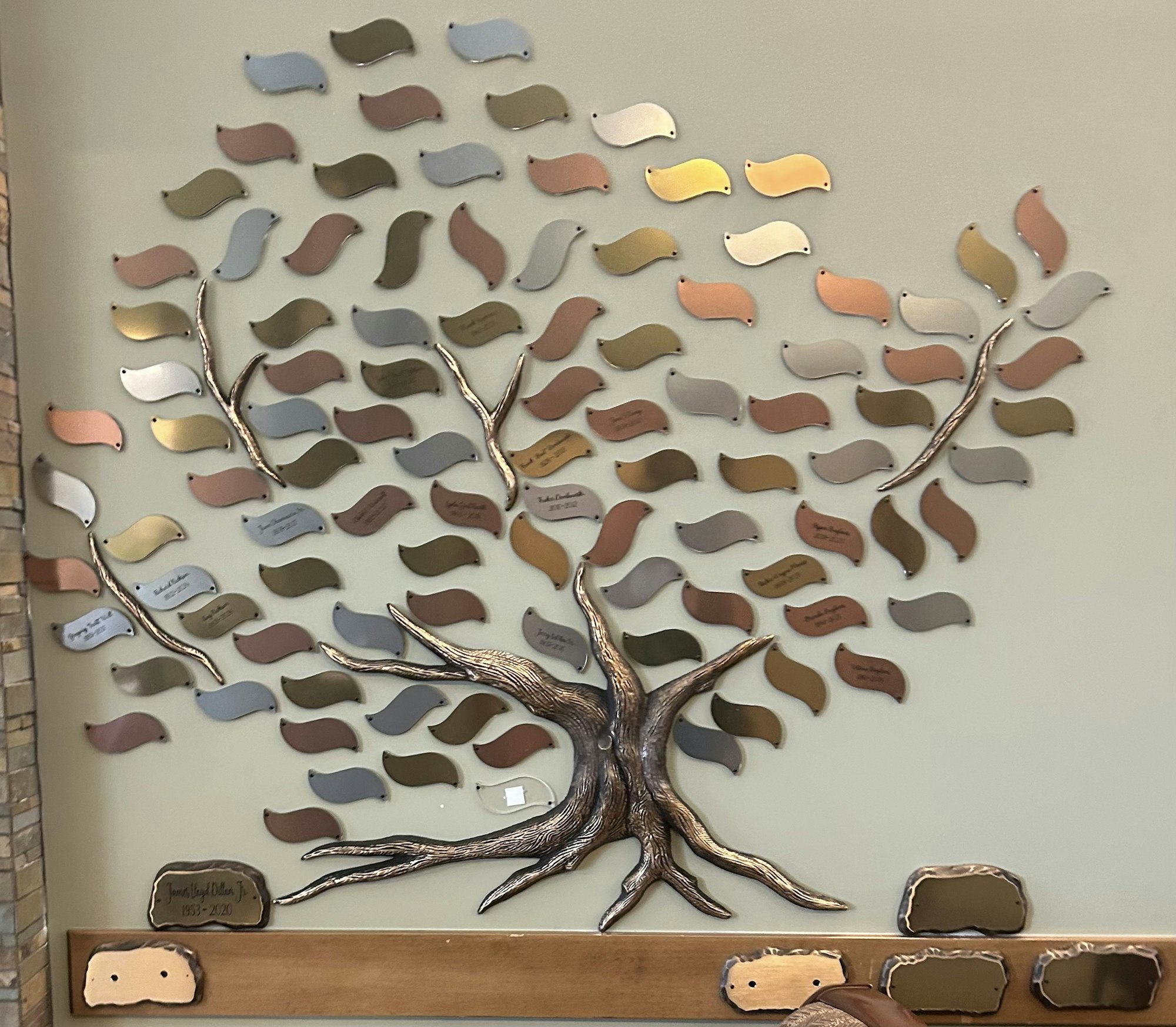 A decorative tree wall art with metal leaves, some engraved with text.