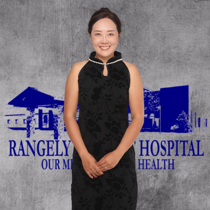 A woman in a black floral dress smiling in front of a "Rangely Hospital" backdrop.