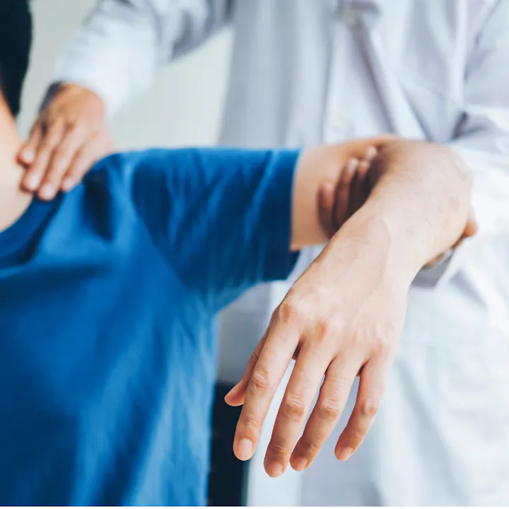 A person in a blue shirt is receiving a shoulder and arm examination or therapy from a professional in a white coat.