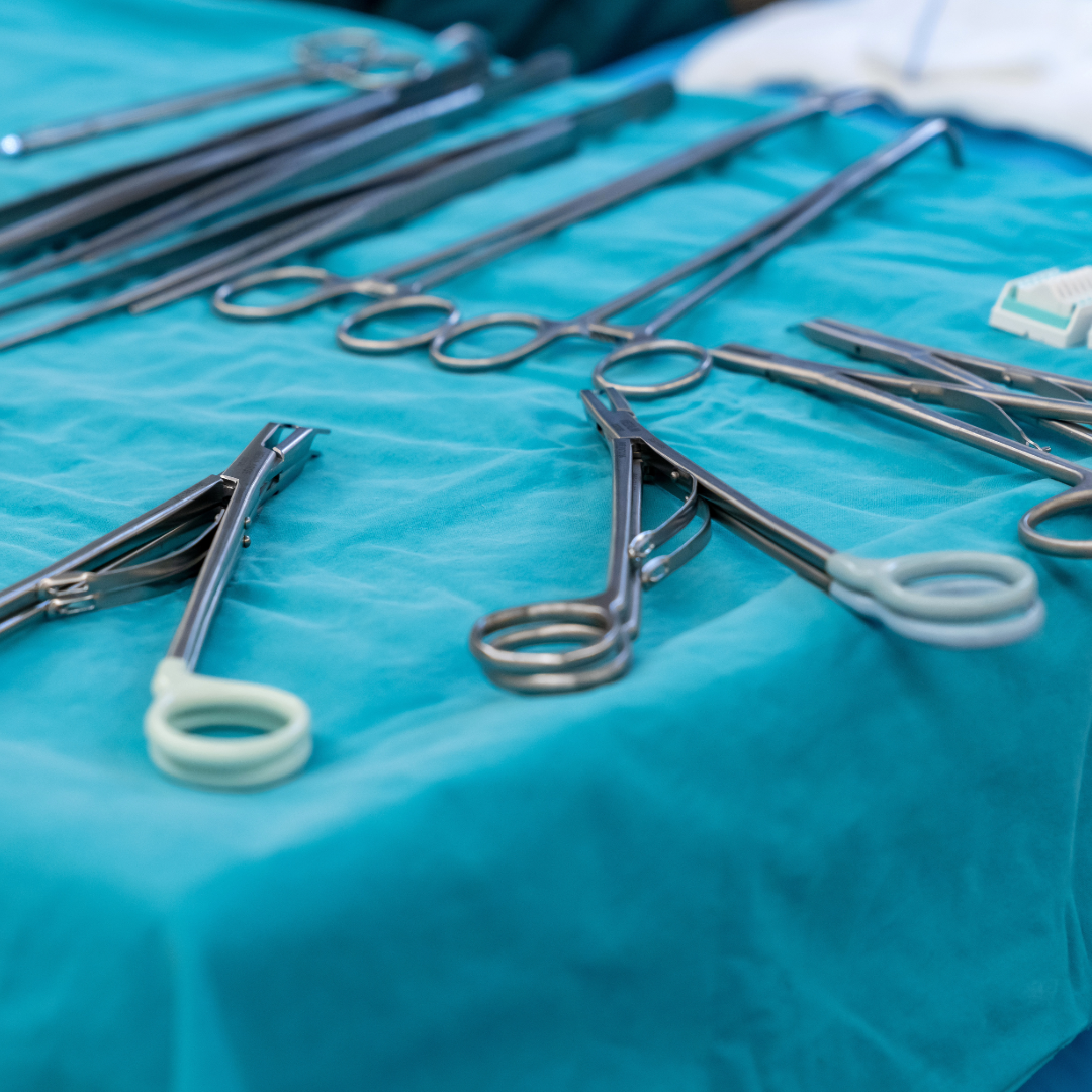 A collection of surgical instruments laid out on a teal tablecloth, ready for a medical procedure.