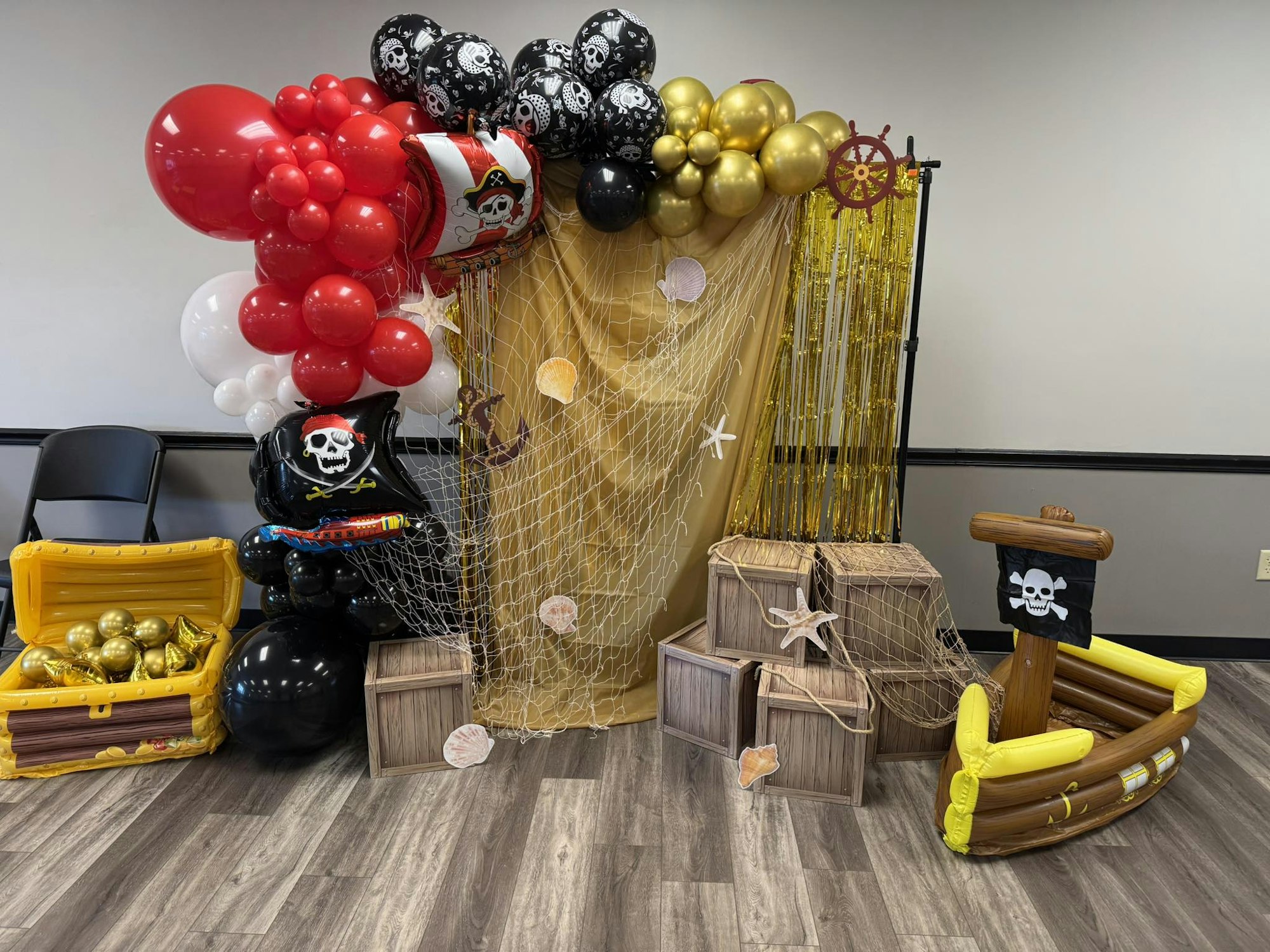 Pirate-themed decorations: balloons, treasure chests, pirate ship, skull flags, and crates.