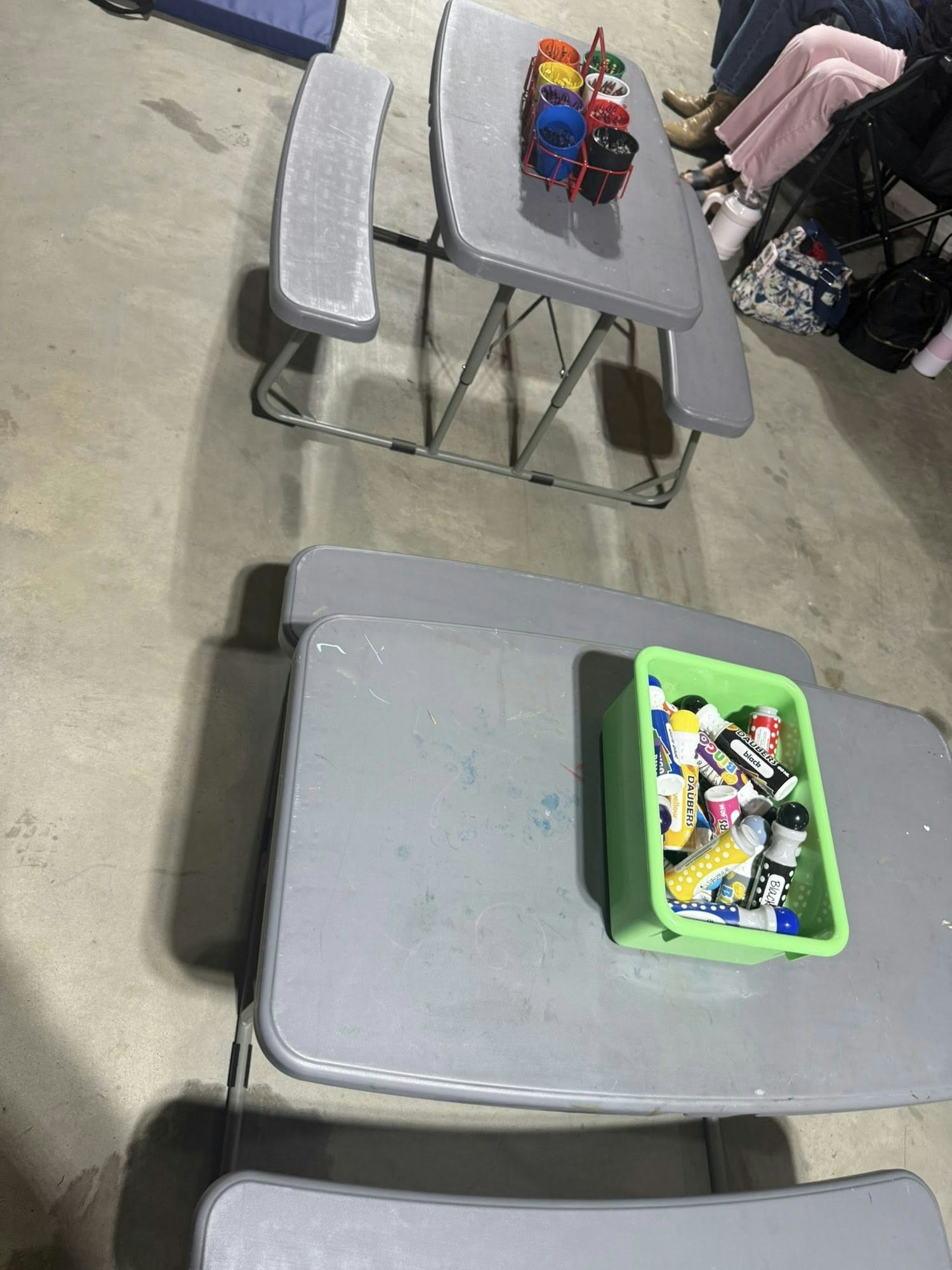Two gray tables with built-in benches, one with bingo daubers and another with craft supplies.