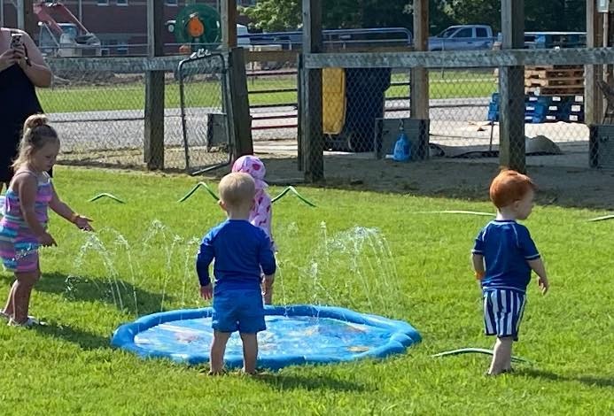 Children playing in a splash pad on the grass, water spraying upwards.