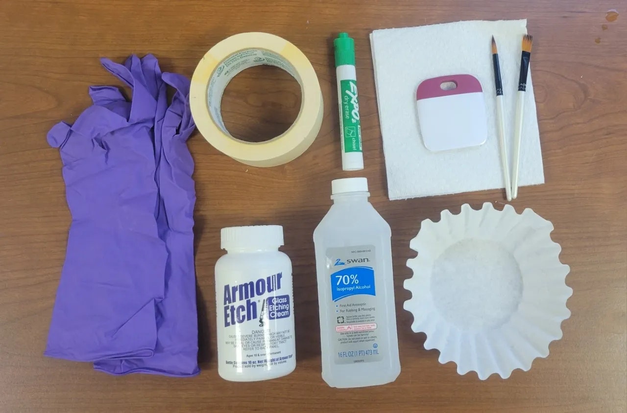 Gloves, masking tape, dry erase marker, felt pad, brushes, craft tools, bottle of Armour Etch, isopropyl alcohol, and a coffee filter.