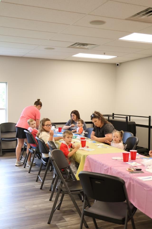 People, including children, are sitting at tables covered with colorful tablecloths, engaging in activities.