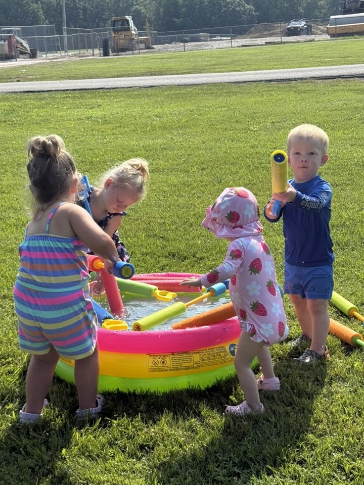 Four children playing with water toys in an inflatable pool on a sunny day.