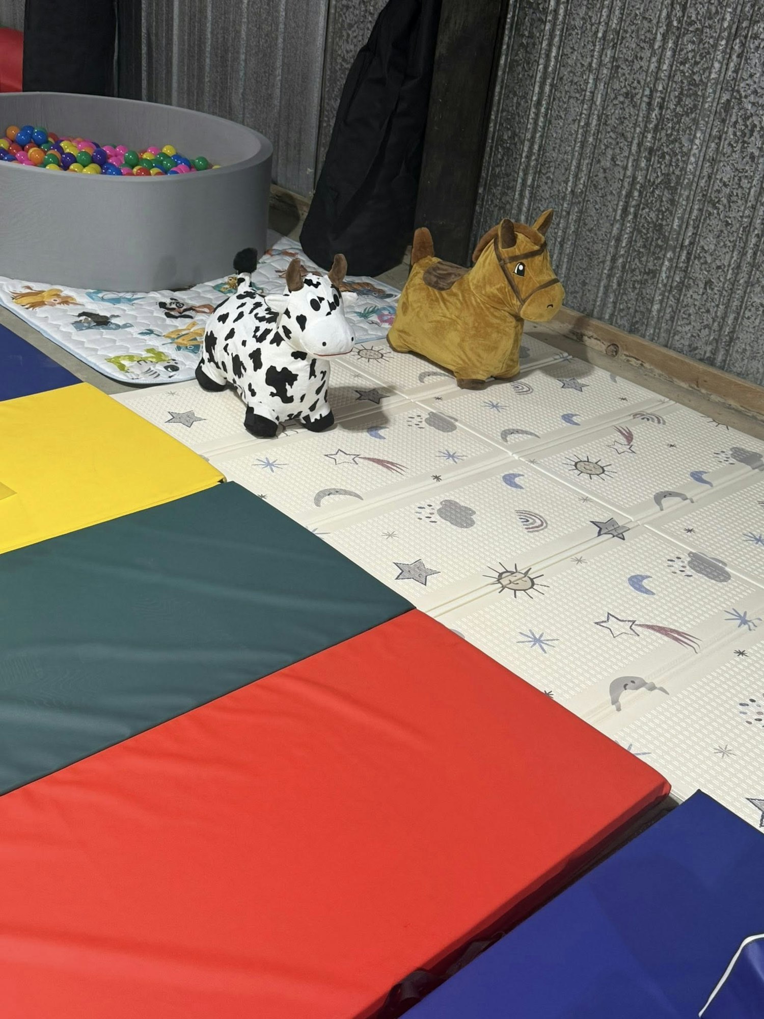 Children's play area with colorful mats, a ball pit, and plush cow and horse toys.