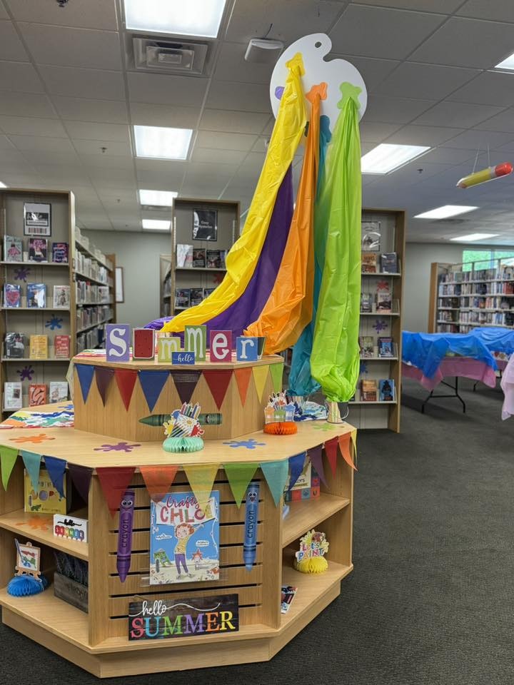 Library display with colorful fabric, "Summer" blocks, bunting, crayons, and books for a summer theme.