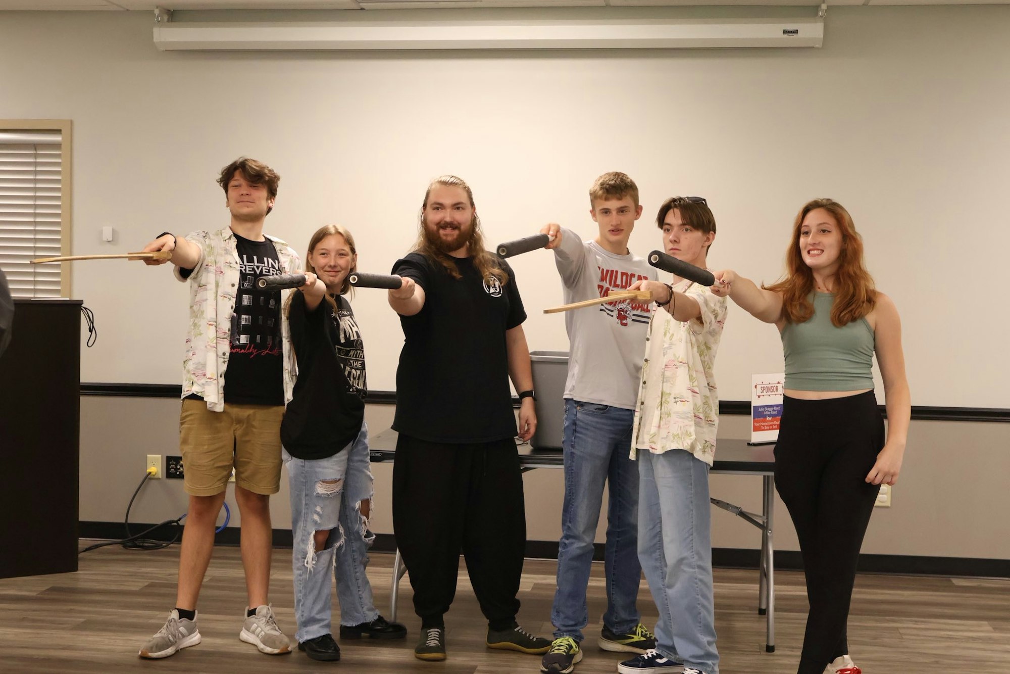 A group of people holding drumsticks, smiling and posing together indoors.