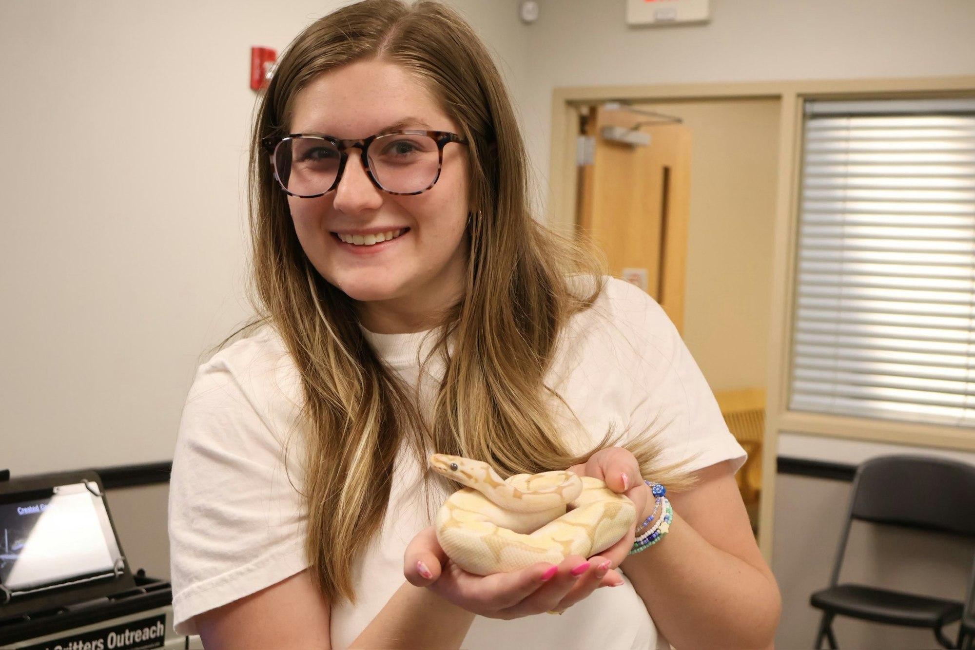 A person smiling and holding a yellow snake in an indoor setting.