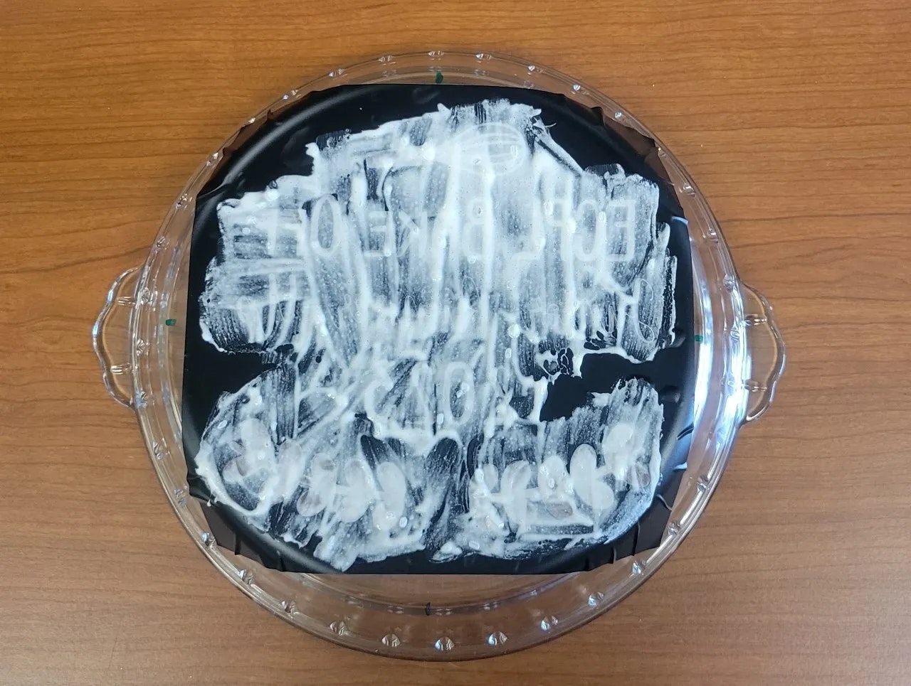 A round glass dish with a black surface covered in randomly spread white paint or cream.