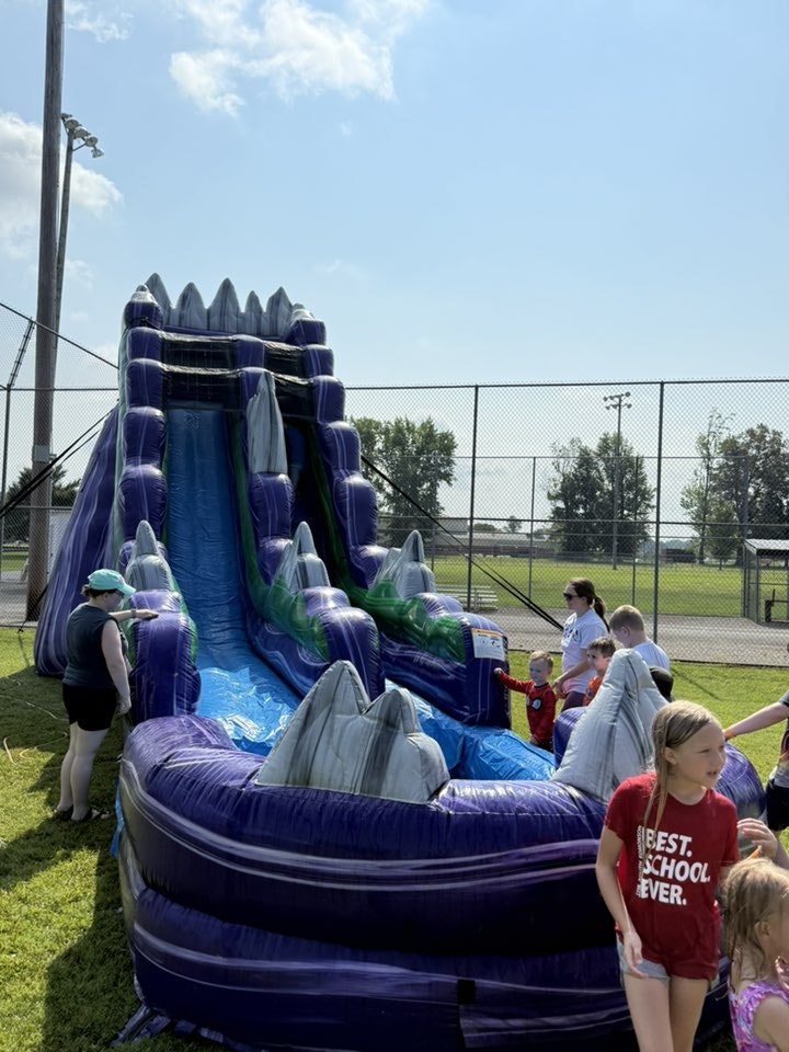 An inflatable water slide with children and adults around it in a park setting.