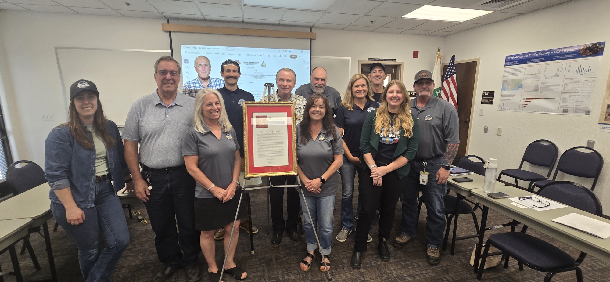 A group of people poses with a framed document, likely celebrating an event or recognition, in a meeting room.