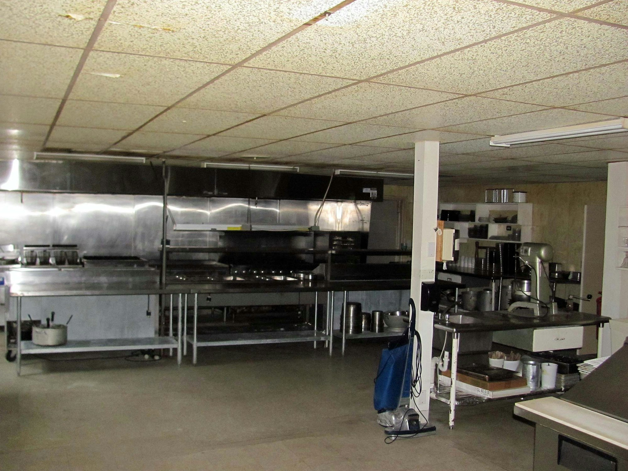 A commercial kitchen with stainless steel counters, cooking equipment, shelves, and a mixer.