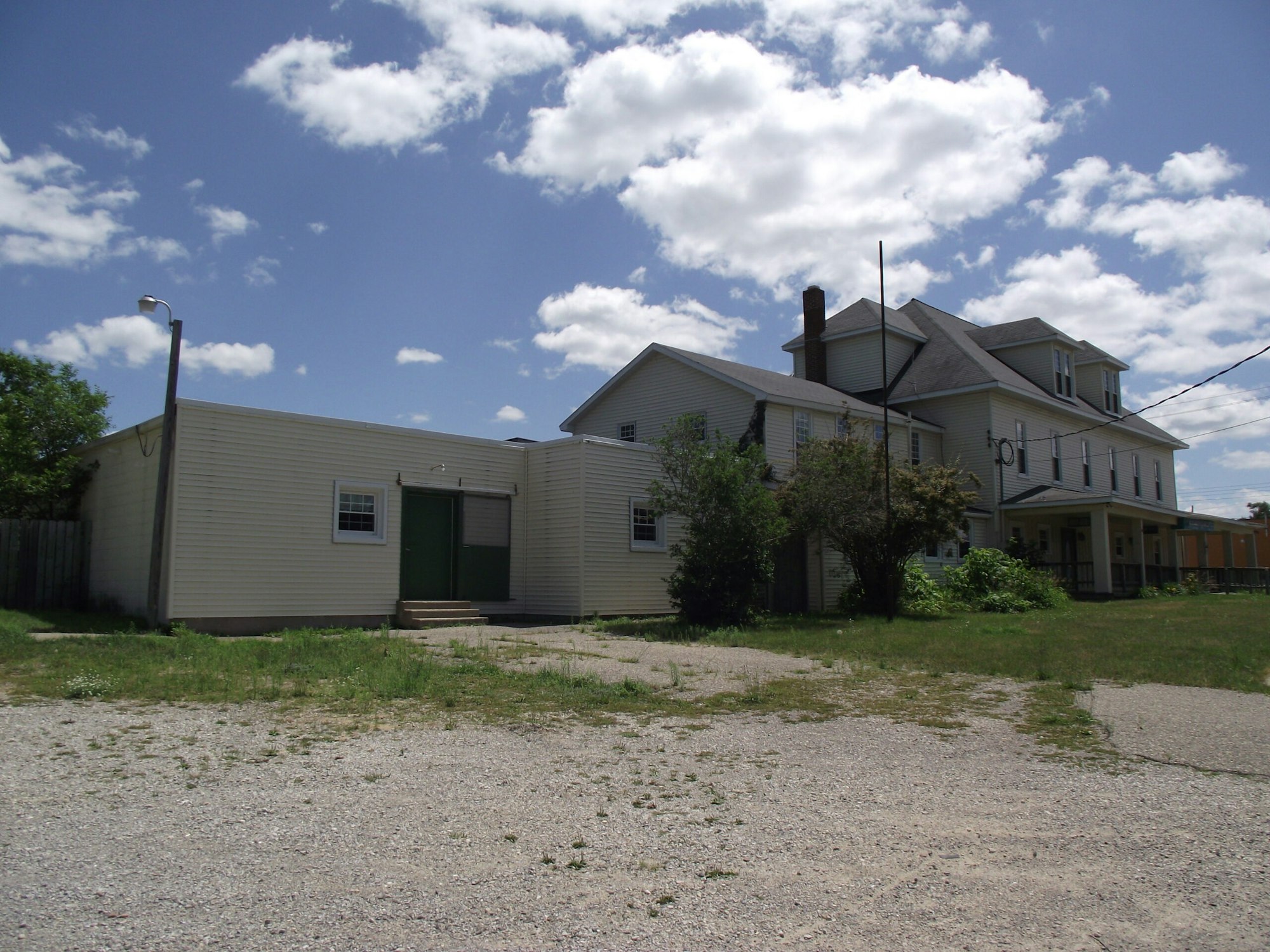 A large, multi-story house with an attached single-story extension under a partly cloudy sky.